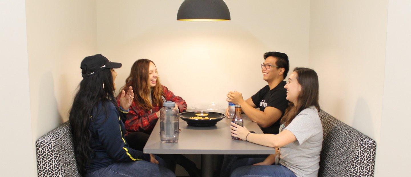 四个学生坐在一张桌子旁，桌子中间放着饮料和食物